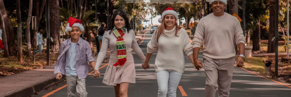 A joyful family walks down a decorated street wearing Christmas hats, symbolizing holiday spirit.